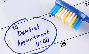 An image featuring a toothbrush with a blue handle resting on a calendar marked dentist appointment at 10 AM, with the words dentist appointment circled around it.